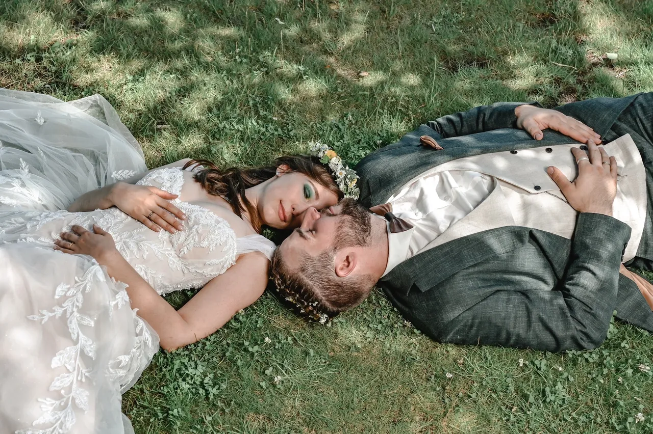 Braut und Bräutigam liegen im Gras und umarmen sich. Romantik am Hochzeitstag.