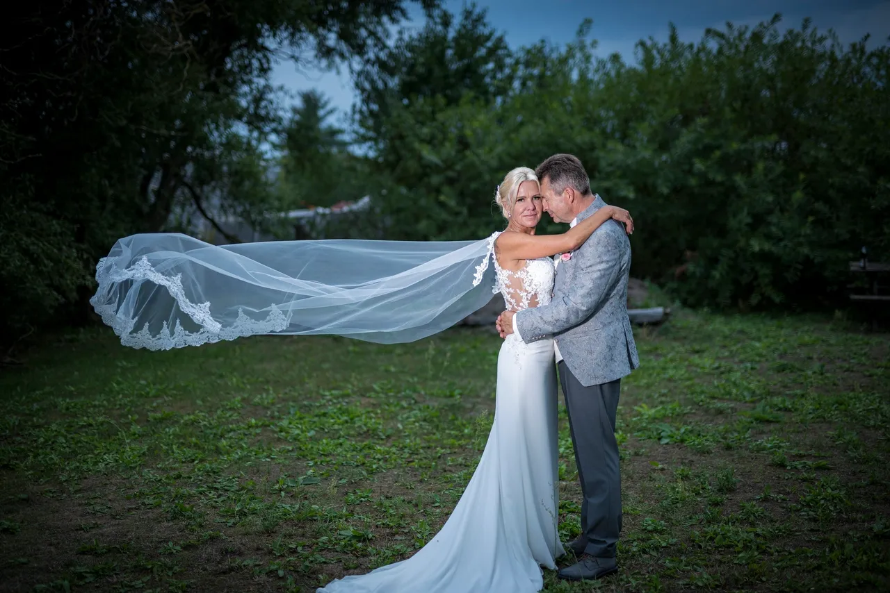 Braut und Bräutigam umarmen sich an ihrem Hochzeitstag, ihr Schleier weht im Wind.