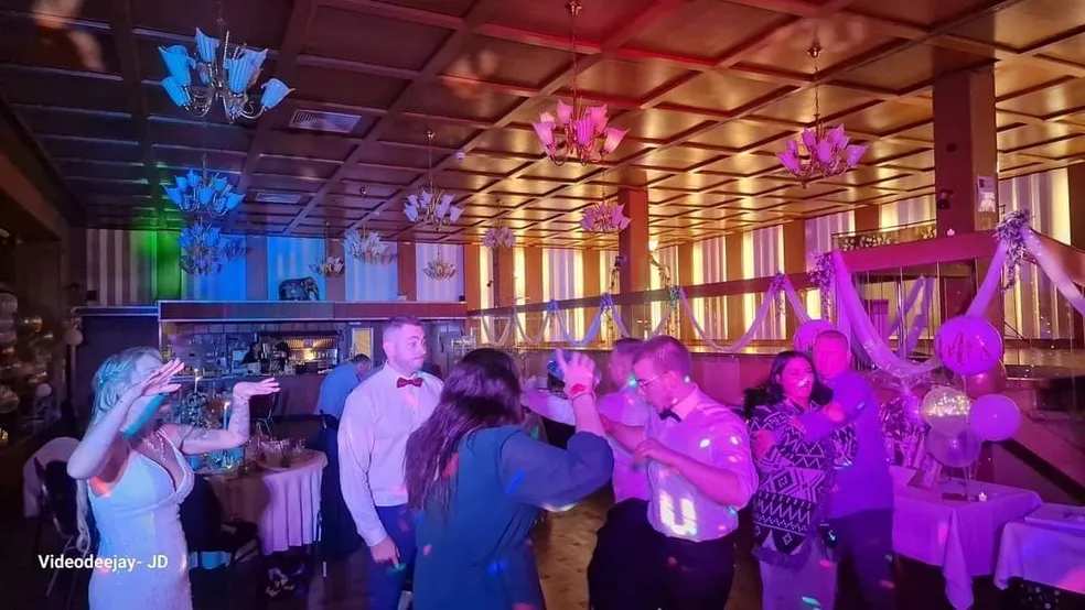 Hochzeitsgäste tanzen beim Empfang, beleuchtet von violetten Lichtern.